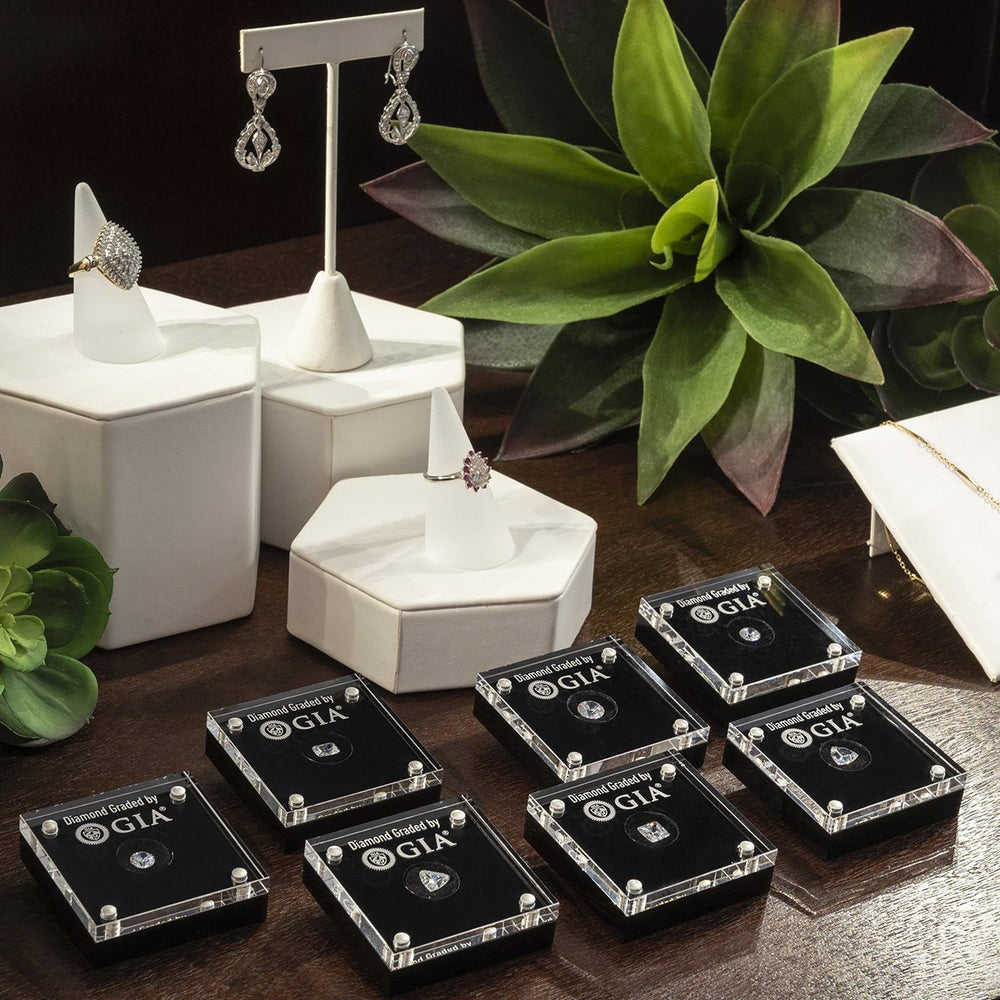 Group of 7 loose diamond display cases on counter with rings, earrings, and succulents